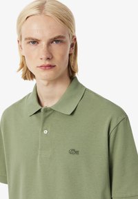 Polo verde con tessuto testurizzato, patta con due bottoni e piccolo logo ricamato sul petto. Maniche corte e design del colletto classico.