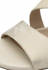 Beige sandál s širokým metalickým páskem s texturovaným lesklým povrchem, hladkým stélkou a minimalistickým designem.