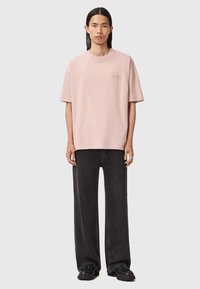 Jasnoróżowa, oversize'owa koszulka bawełniana z krótkim rękawem i okrągłym dekoltem; posiada subtelne logo na lewej piersi. Połączona z czarnymi dżinsami.