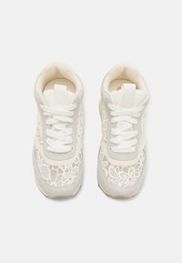 Des chaussures de sport blanches avec un dessus en maille, des accents en suede, un bout rond et des lacets blancs. Le design est léger et texturé.