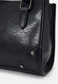 Coin de sac en cuir noir texturé avec rivets métalliques et détails de couture sur une surface lisse et des bords arrondis.