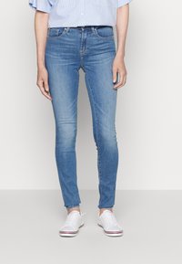 Jeans skinny de color azul claro con cinco bolsillos, un acabado ligeramente desgastado y un dobladillo sin acabar, combinados con zapatillas blancas.