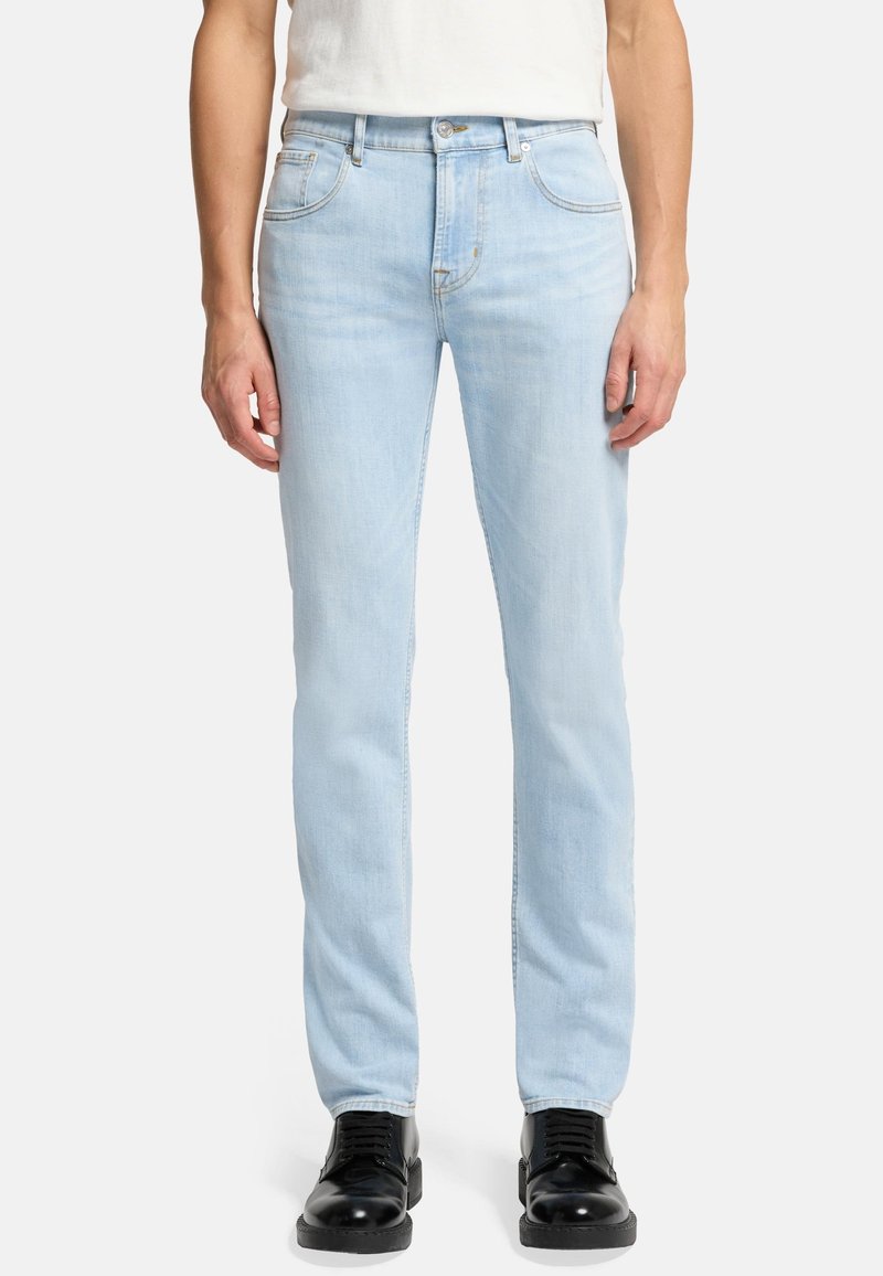 Jasnoniebieskie dżinsy o slim fit, z pięcioma kieszeniami, zapięciem na guzik i kontrastowymi przeszyciami. Zestawione z czarnymi butami.