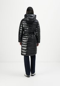 Cappotto imbottito nero con finitura lucida, cappuccio e vita accentuata da una cintura. Presenta un motivo a righe orizzontali e design di lunghezza media.