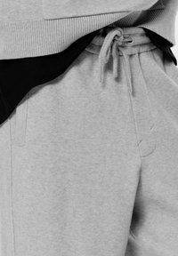 Sivé tepláky vyrobené z mäkkého materiálu, s elastickým pásom na šnúrku a bočnými vreckami. Dizajn je neformálny a funkčný.