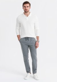 Vit långärmad polo, grårandiga byxor och vita sneakers. Byxorna har en justerbar dragsko i midjan och fotmanschetter.