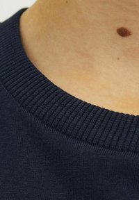 Tamsiai mėlynas megztinis su apykakle, turintis račiuotą tekstūrą, su lygia iškirpte ir priartinta audinio detale.