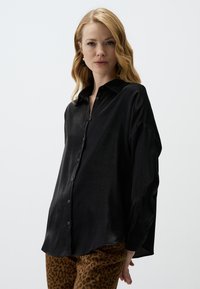 Black satin button-up shirt with a collared neck, relaxed fit, and long sleeves, paired with brown leopard print pants.