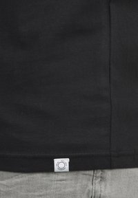 Schwarzes Baumwoll-T-Shirt mit glatter Textur, ausgestattet mit einem kleinen weißen Etikett am unteren Saum und einem klassischen geraden Schnitt.
