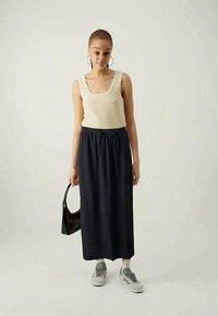 Tejelt krémszínű pántos felső, texturált mintával, sötét hosszú szoknyával párosítva. Szürke sportcipők és egy fekete táska egészíti ki a szettet.