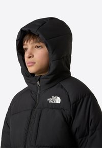 Fekete szigetelt pehelydzseki kapucnival, elülső cipzárral, steppelt mintával és fehér logóval a bal felső mellrészen.