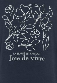 Marineblauwe stof met witte bloemcontouren. Tekst luidt "LA BEAUTÉ EST PARTOUT Joie de vivre." Strak ontwerp, moderne typografie en eenvoudige grafische elementen.