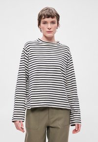 T-shirt de manga longa às riscas em creme e preto, com decote redondo e corte descontraído. Combinado com calças verde-oliva. Textura de tecido suave.