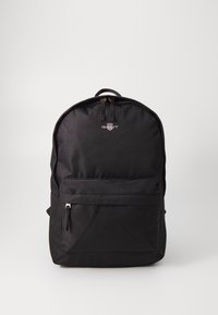 Sac à dos en tissu noir avec une forme arrondie, doté d'une poche zippée à l'avant et d'une poignée sur le dessus. Comprend un logo de marque sur le devant.