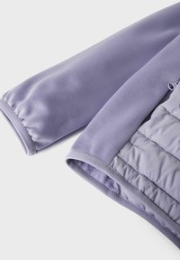 Helllila Jacke aus glattem Stoff, mit gesteppter Innenfütterung und Fischgrätenmuster am Ärmel und Saum. Mit Reißverschlussverschluss.