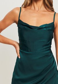 Satin teal klänning med tunna band, med en draperad halsringning och en figurnära midja som övergår till en mjukt samlad kjol.