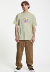 Lys grøn bomulds T-shirt med et farverigt grafisk tryk på brystet, parret med brune corduroy bukser og sorte sneakers.