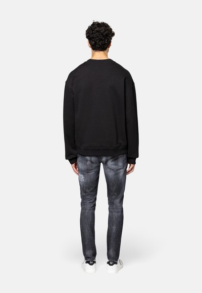 Zwarte oversized sweatshirt met ronde hals, gecombineerd met grijze versleten spijkerbroek en witte sneakers, van de achterkant bekeken.