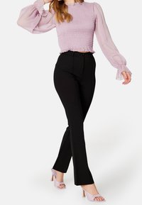 Lilačový smockovaný crop top s průhlednými volnými rukávy, spárovaný s černými flared kalhotami s vysokým pasem a světle fialovými otevřenými podpatky.