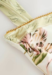 Halványszínű zöld szövet, amelyen "Tulpa" felirat és részletes rózsaszín-zöld virágminta látható, arany gyöngy szegéllyel díszítve.