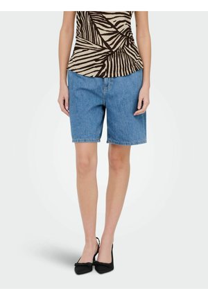 Femme portant un short en jean bleu mi-long, un haut beige et noir à motifs, et des escarpins noirs à bout pointu avec des détails de nœud.
