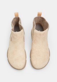 Botas beige tipo slip-on hechas de un suave tejido texturizado con laterales recortados y una lengüeta de cuero marrón, con suela de goma.