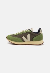 Grønne og brune sneakers laget av semsket skinn og mesh, med kremfargede detaljer, en gummisåle, og "V"-merke på siden og hælen.