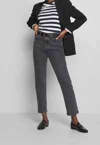 Svarta högmidjade jeans med rak passform, tillsammans med en marinblå och vit randig skjorta och en svart kavaj. Svarta loafers fulländar looken.