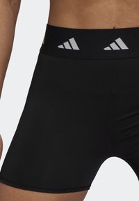 Mustat urheilushortsit, joissa on sileä pinta, ja jotka ovat varustettu leveällä mustalla vyötärönauhalla, jossa on valkoista brändäystä ja hienovaraisia ompeluyksityiskohtia.