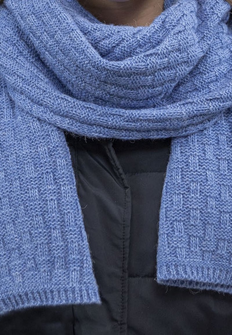 Personne portant une écharpe texturée bleu clair enroulée autour du cou par-dessus une veste matelassée noire.
