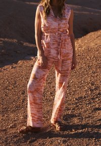 Combinaison rayée rose et orange avec col, fermeture à boutons et ceinture à nouer. Comprend un pantalon à jambes larges et deux poches avant.