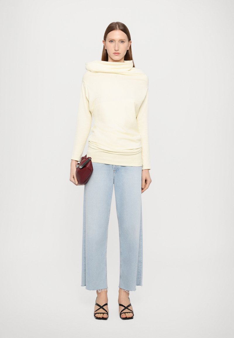 Ljusgul långärmad topp med en cowl-hals, parat med ljusblå vida jeans, svarta sandaler med remmar och en liten bordeauxfärgad handväska.