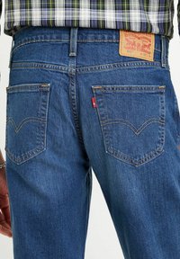 Jeans in denim blu con taglio dritto, caratterizzati da cuciture a contrasto, doppie tasche posteriori e un'etichetta del marchio in pelle marrone sulla vita.