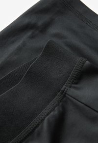 Czarna tkanina sportowa o gładkiej fakturze, z żebrowanym paskiem w talii i szwami płaskimi dla wygody i elastyczności.