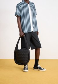 Camisa de manga corta a rayas en azul con rayas blancas, combinada con pantalones cortos negros. Sosteniendo un bolso negro acolchado. Zapatillas negras completan el look.