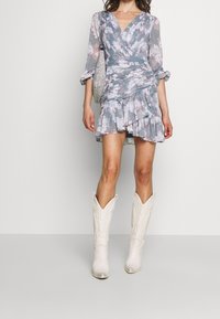 Ljusblå miniklänning med blommönster, volanger i nederkant, långa ärmar och en figurnära design. Matchad med vita cowboystövlar och en glittrande väska.