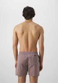 Bañadores de hombre en tejido color malva claro, con cinturilla elástica y detalle de bolsillo trasero, textura suave y sin patrones visibles.