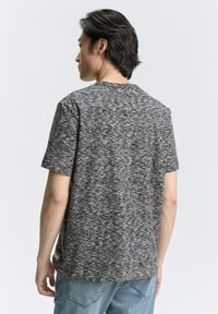 Camiseta de manga corta en gris y negro con un patrón abstracto texturizado. Cuello redondeado y corte relajado, combinada con jeans de color azul claro.