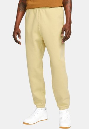 Light yellow sweatpants with elastic waistband and cuffs, made from soft fabric. Paired with white sneakers featuring a gum sole.