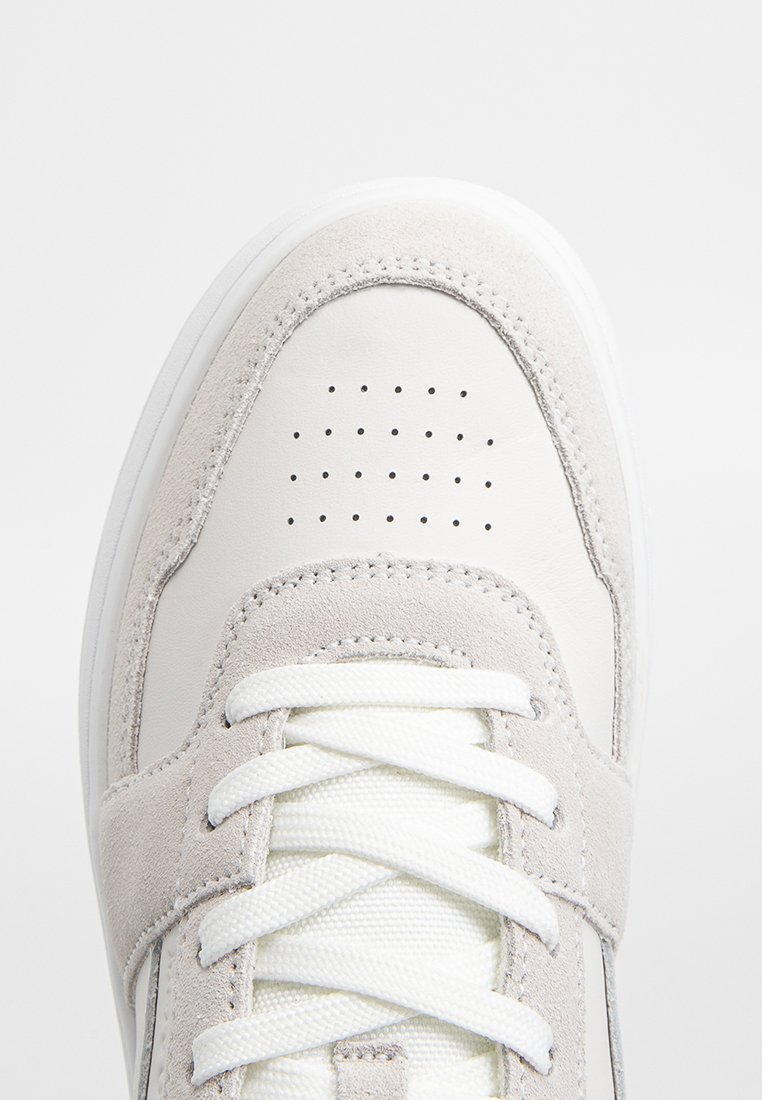 Białe sneakersy z jasnoszarymi akcentami z zamszu, okrągłym noskiem i perforowanymi detalami. Posiadają białe sznurowadła oraz teksturowaną podeszwę zapewniającą przyczepność.
