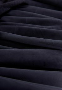 Tuvplāns ar tumši zilu krokotu audumu ar smalku sieta faktūru un slāņainām krokām.