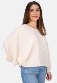 Lockere, cremefarbene Bluse aus strukturiertem Stoff mit Fledermausärmeln und Spitze am Saum. Tragen mit hellblauen Jeans.