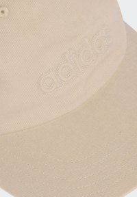 Gorra de béisbol beige con tela texturizada, visera curvada y logo bordado de "adidas" en hilo a juego.