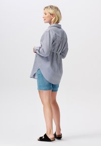 Randig skjorta med långa ärmar och krage, med en böjd nederkant och knytdetalj bak, i kombination med denimshorts och svarta slidesandaler.