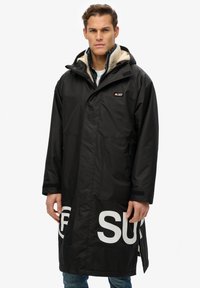 Abrigo negro impermeable con capucha, forro interior acolchado, gran logo blanco en el dobladillo y bolsillos laterales, con un diseño de corte recto.