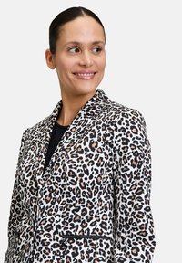 Jassen van luipaardprint in wit, zwart en bruin, met een notch-lapel, een voorzak met rits en een getailleerde pasvorm. Soepele stoftextuur.