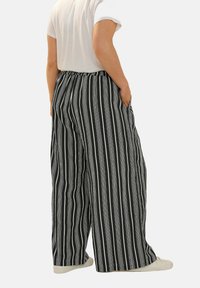 Breda byxor i lätt tyg med vertikala svart- och vitrandiga mönster, med elastisk midja och sidofickor.