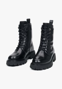 Černé kožené kotníkové boty s texturovaným povrchem, šněrovacím designem a bočním zipem. Silná gumová podrážka s hlubokým vzorem pro lepší přilnavost.