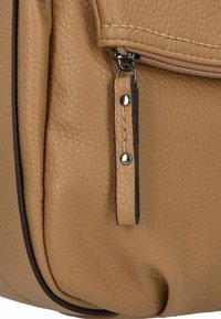 Nahaufnahme einer tanfarbigen Lederhandtasche mit strukturiertem Oberflächenmaterial, einem Reißverschluss und einem detaillierten Tragegurt mit silbernen Hardware-Akzenten.