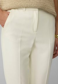Hoge taille crème broek van een gladde stof met zijzakken en plooien, voorzien van een schoon ontwerp en een subtiele glans.